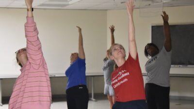 Sarah Rhoads, dean of the UAMS College of Nursing, and four other participants stretch their arms toward the ceiling during the yoga session.