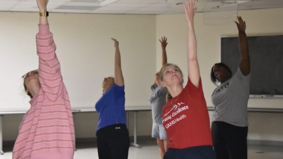 Sarah Rhoads, dean of the UAMS College of Nursing, and four other participants stretch their arms toward the ceiling during the yoga session.