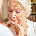 Older woman looking down with her chin resting on her hand