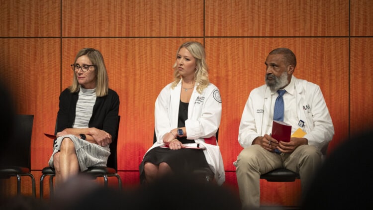 As seen from one of the rows in the auditorium, Dean Susan Long, left, Maggie Grappe and Billy Thomas sit on stage and listen as Edward Williams delivers his opening remarks at the ceremony. 