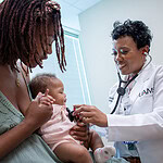 mother holds baby as physicians holds stethescope to check the baby's heart rate