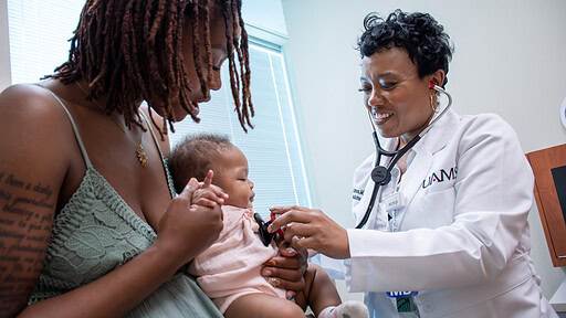 mother holds baby as physicians holds stethescope to check the baby's heart rate
