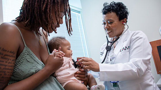 mother holds baby as physicians holds stethescope to check the baby's heart rate