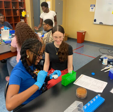 Two female HCOP Academy students smile as they sit at a lab table during an activity at Southern Arkansas University in Magnolia.