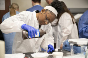 High school student Aria Bursey pours liquid into a container during a lab