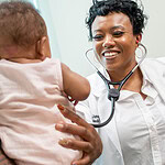 C'Asia James, M.D., smiles and holds a stethescope to a baby.