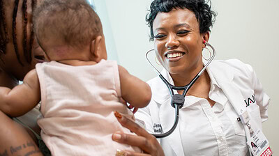 C'Asia James, M.D., smiles and holds a stethescope to a baby.