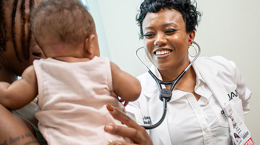 C'Asia James, M.D., smiles and holds a stethescope to a baby.