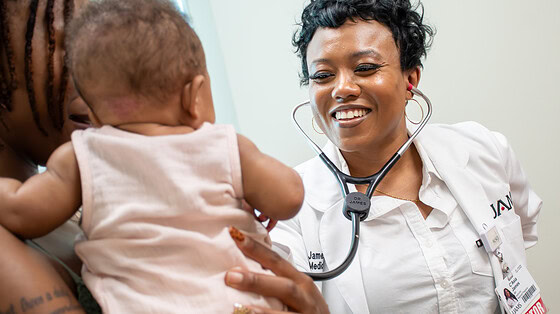 C'Asia James, M.D., smiles and holds a stethescope to a baby.