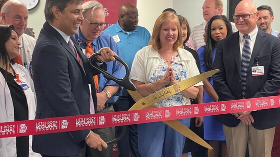 Rohit Dhall, M.D., chair of the UAMS Department of Neurology, prepares to cut the ribbon officially opening the UAMS Health Neurology Clinic in the Doctors Building for multiple sclerosis and headache patients as Michelle Krause, M.D., senior vice chancellor of UAMS Health, and Robert D. Robinson, M.D., dean of the UAMS College of Medicine and executive vice chancellor of UAMS, look on from the front row.