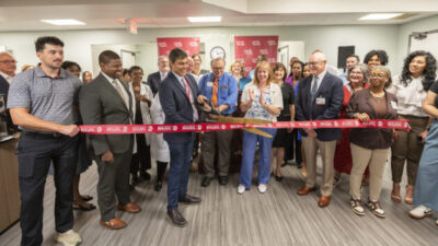 Rohit Dhall, M.D., prepares to cut the ribbon officially opening the UAMS Health Neurology Clinic in the Doctors Building as Jonathan Goree, M.D., (left of Dhall, front row), and Scott Lucchese (right of Dhall, front row), Michelle Krause, M.D., and Ron Robertson, M.D., look on.