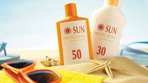 Photo of sunscreen bottles and sunglasses sitting on a blanket at the beach