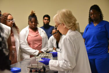 Students gather around a table where a UAMS employee demonstrates how medications are compounded.