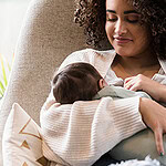 A smiling woman is shown breastfeeding her baby.