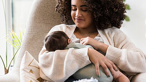 A smiling woman is shown breastfeeding her baby.