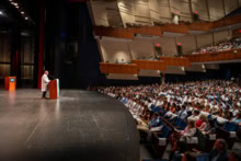 College of Medicine Dean Ron Robertson, M.D., welcomes the new medical students in a cavernous auditorium. Wide-angle image shows Robertson at lectern and part of crowd in front of him.