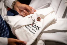 A close-up photo of one student's white coat, which is being unfolded.