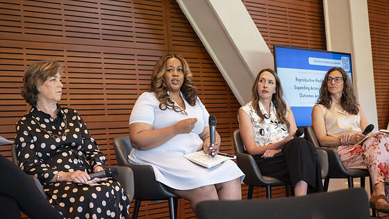 Four women who are on a panel on reproductive health sit in chairs onstage discussing ways to improve access and health outcomes. Keesa Smith-Brantley, executive director of Arkansas Advocates for Children and Families, holds the microphone and is speaking.