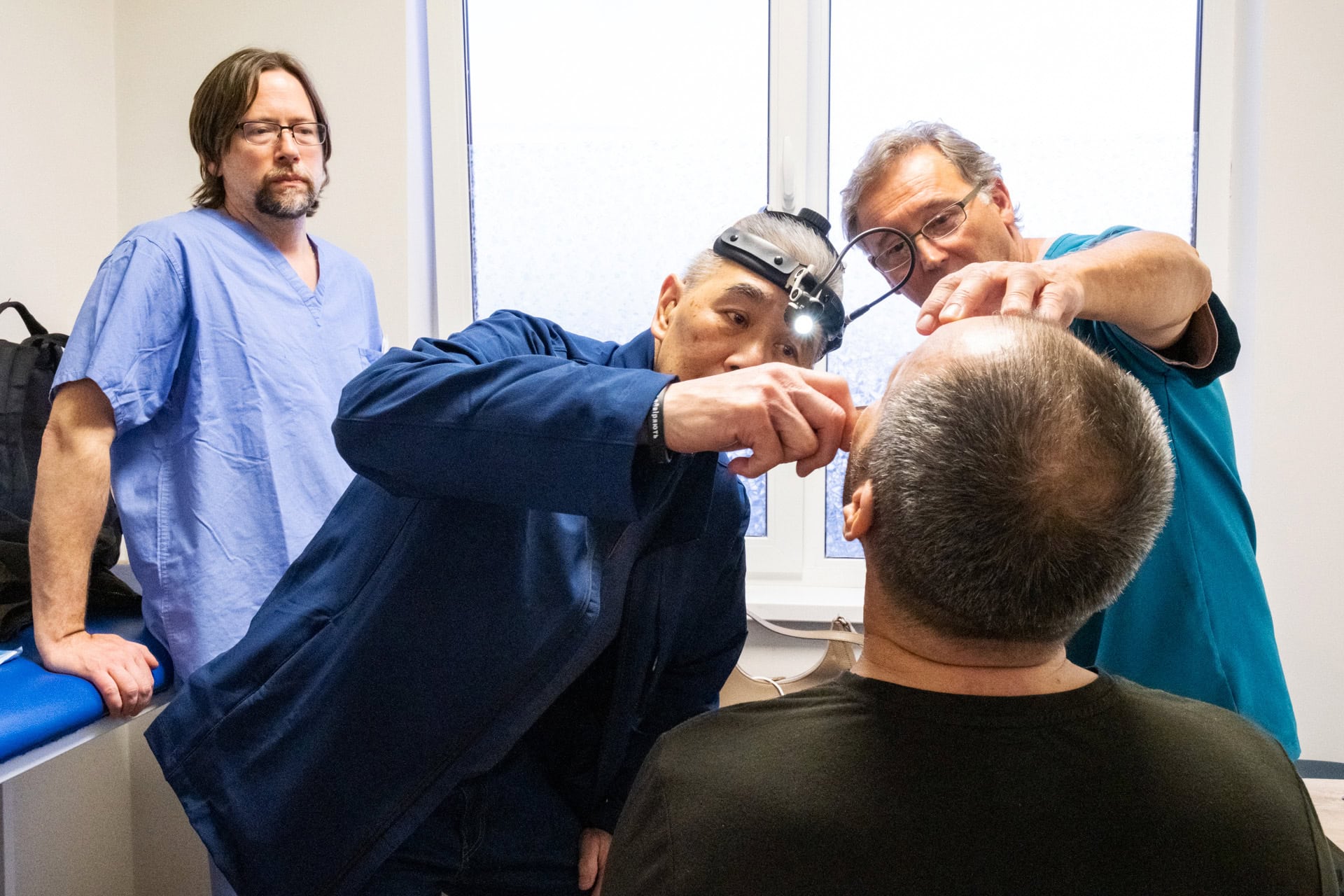 Suen, center, along with physicians Mark Hnatiuk, left, and Roman Bukachevsky examines the skull and face of a Ukrainian man injured in the war there.