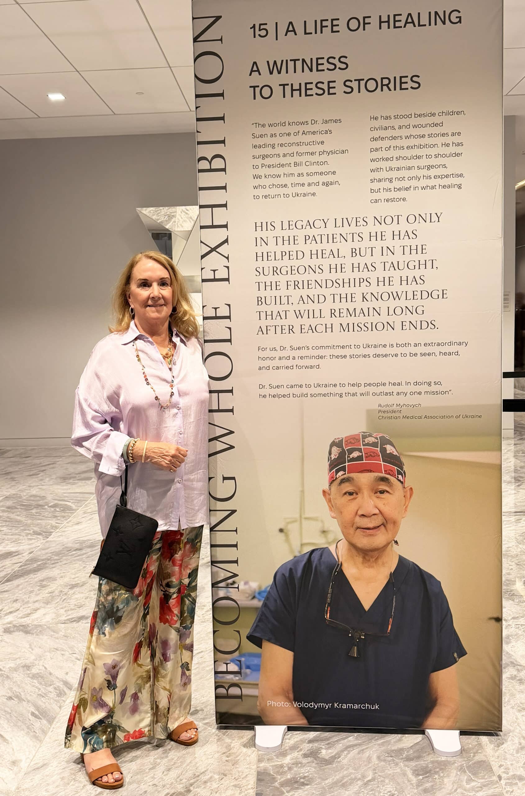 Karen Suen, wife of James Suen, stops for a moment in Dallas to stand next to a large poster honoring her husband.