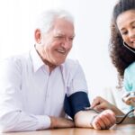 An older man smiles as he's having his blood pressure measured by a woman in this stock image.