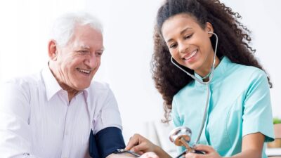 An older man smiles as he's having his blood pressure measured by a woman in this stock image.
