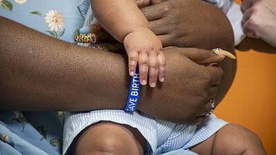 An up-close shot of a woman wearing an I Gave Birth bracelet and holding an infant.