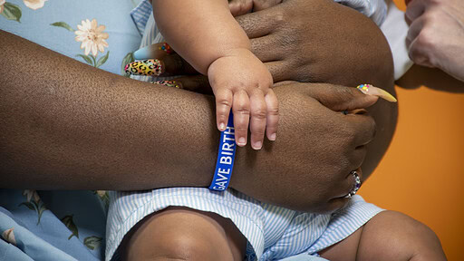 An up-close shot of a woman wearing an I Gave Birth bracelet and holding an infant.