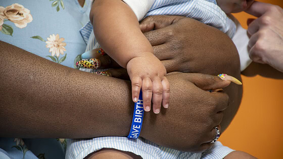 An up-close shot of a woman wearing an I Gave Birth bracelet and holding an infant.