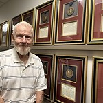 Tribell stands beside a wall of framed medallions in the UAMS College of Medicine administrative office.