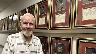 Tribell stands beside a wall of framed medallions in the UAMS College of Medicine administrative office.