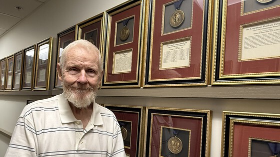 Tribell stands beside a wall of framed medallions in the UAMS College of Medicine administrative office.